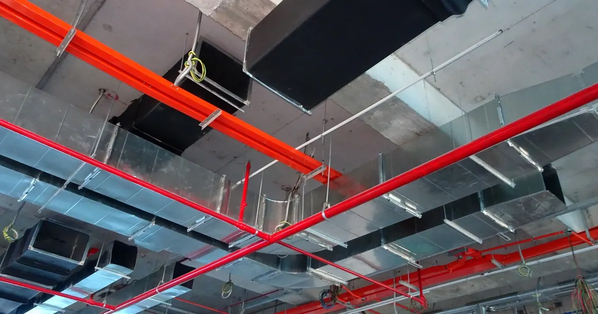 Exposed ceiling services in a building: galvanised air ducts, red sprinkler pipes and cable conduit
