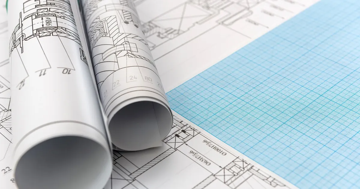 Rolled technical drawings lying on flat engineering sheets beside a sheet of blue graph paper