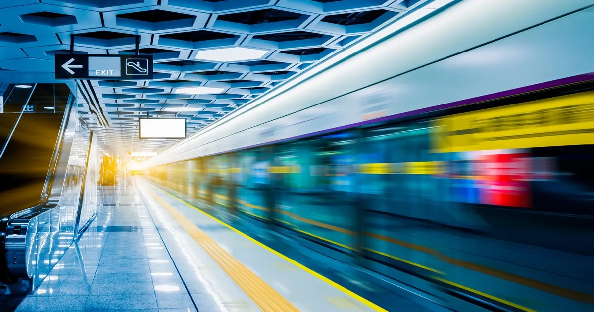 A train blurring past a metro platform, with an exit sign overhead and a yellow line along the edge