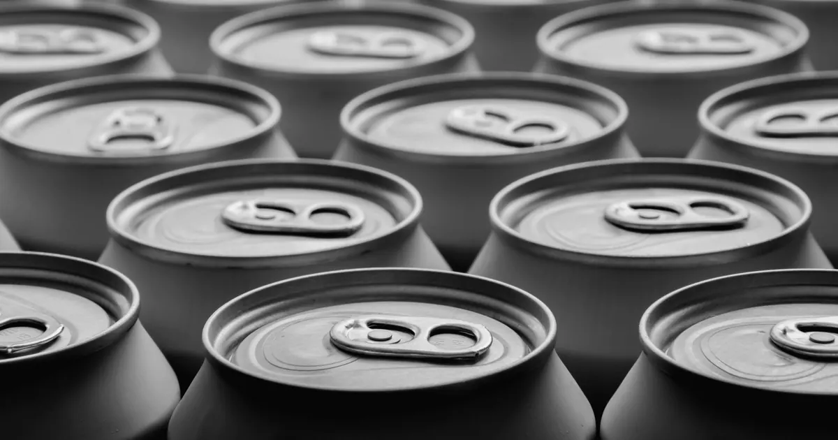 Rows of identical unlabelled aluminium drink cans seen from above in black and white