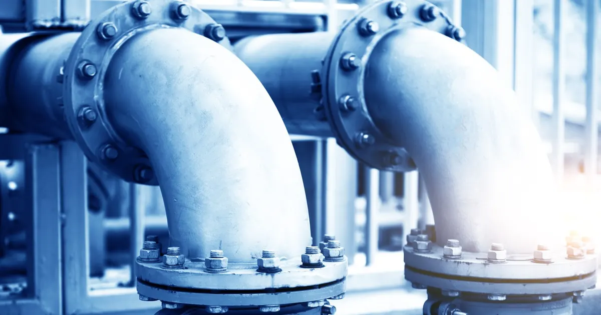 Large bolted flange joints on curved industrial water pipes in a plant room, tinted blue