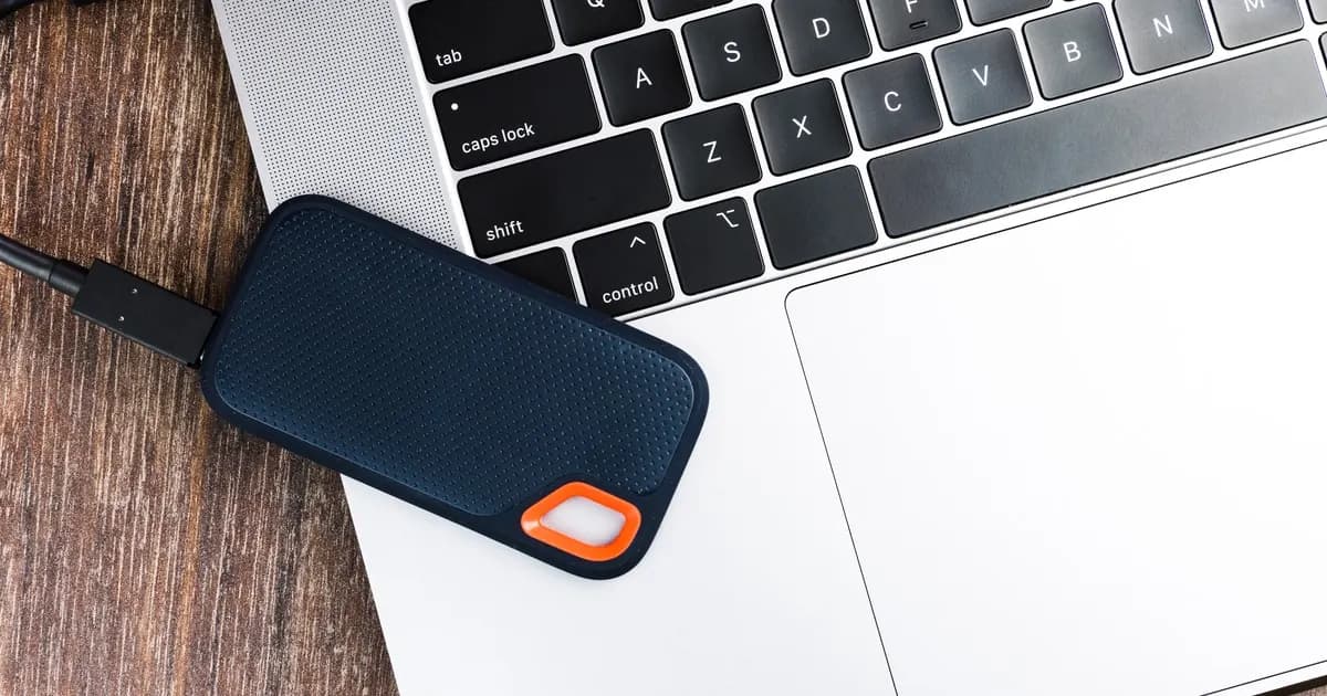 A portable external SSD with a USB cable resting on a laptop keyboard and trackpad