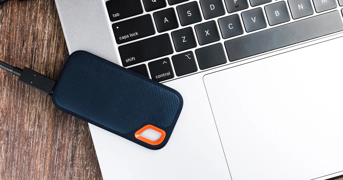 A portable external SSD with a USB cable resting on a laptop keyboard and trackpad